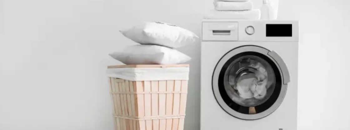 Pillows in a laundry basket next to a washing machine.