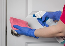 A professional maid wearing blue nitrile gloves spraying pink cleaning cloth.