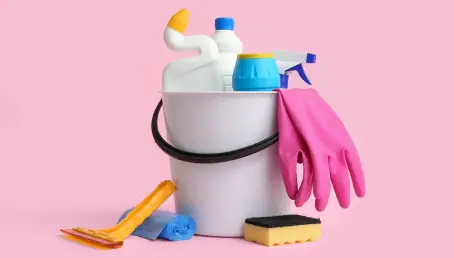 Bucket with different cleaning supplies on pink background