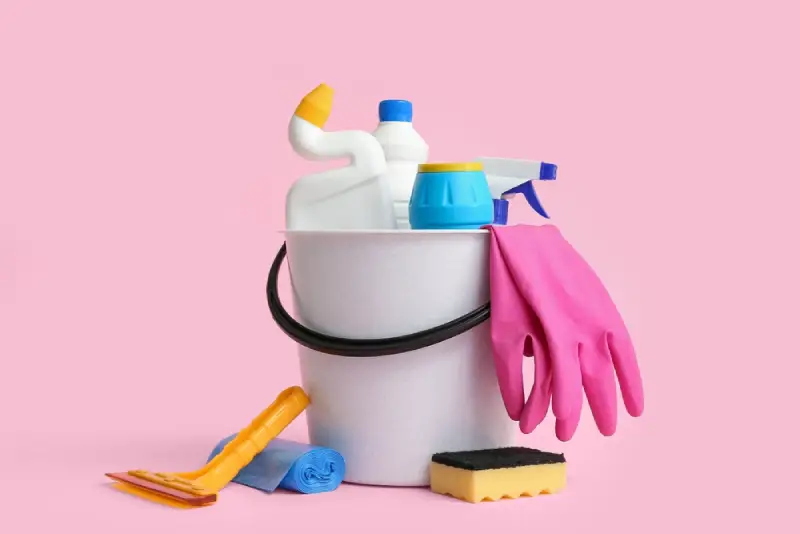 Bucket with different cleaning supplies on pink background