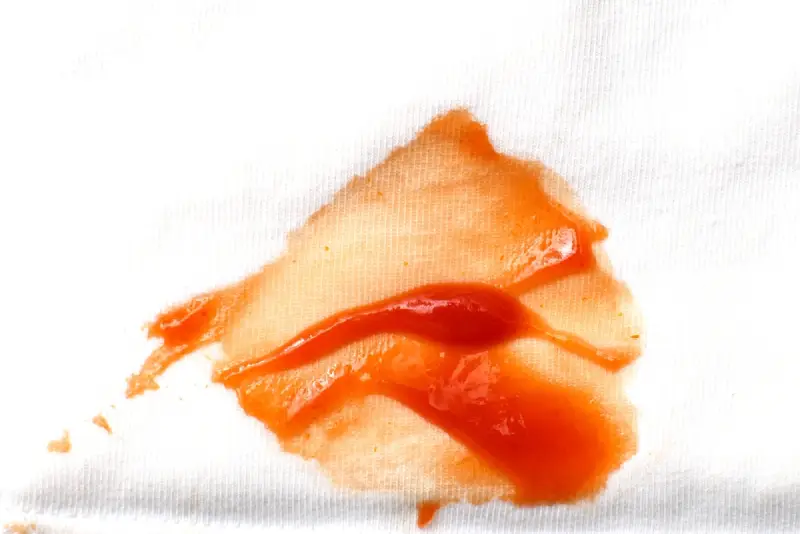A ketchup bottle spilling onto a white cotton shirt.