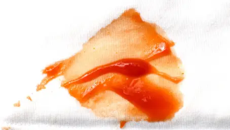 A ketchup bottle spilling onto a white cotton shirt