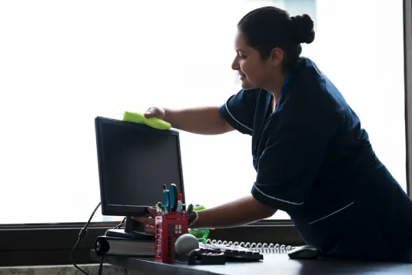 A cleaning professional wiping down a computer monitor