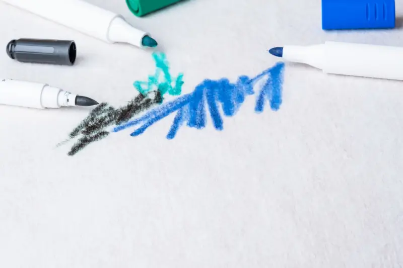 Blue, black, and teal markers leaving stains on white carpet.