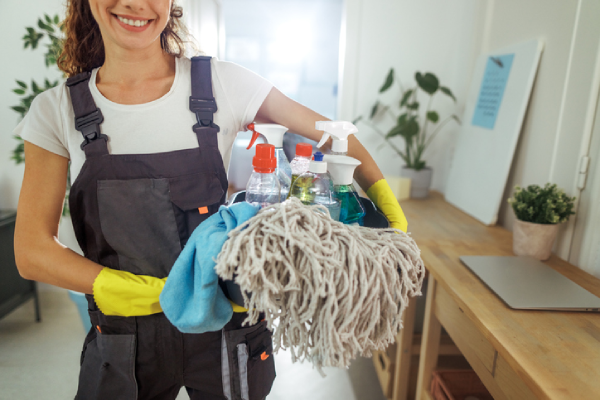 A cheerful woman in overalls holding cleaning supplies