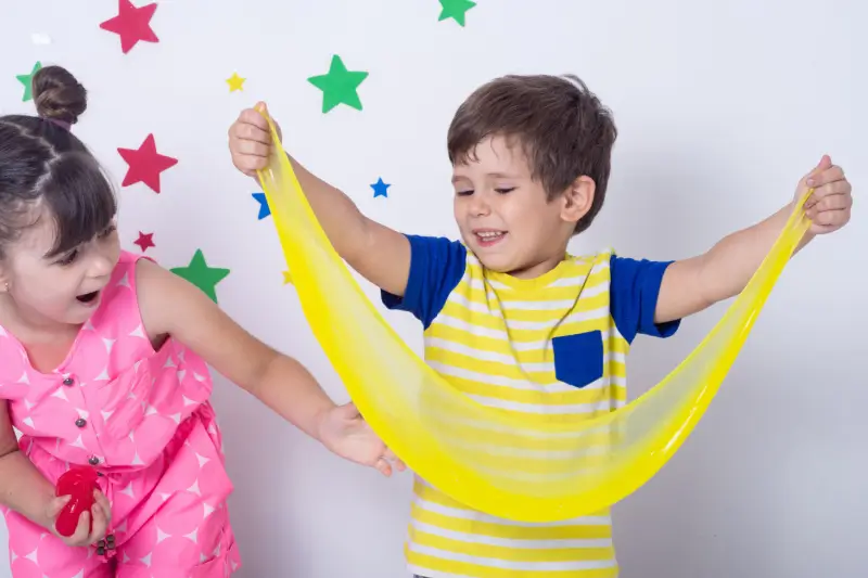 Two kids playing with yellow and red slime.