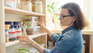 Adult woman organizing items in a kitchen pantry with wooden shelves