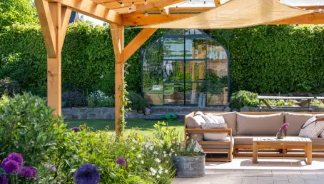 A covered patio in a sunny garden with outdoor furniture.